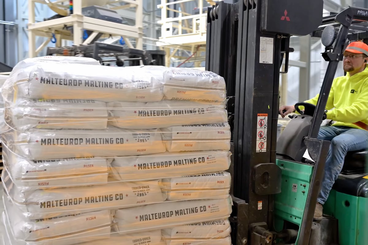 A worker skillfully operates a forklift, transporting a pallet of Malteurop malting company bags.